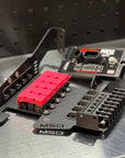 A close-up of an MSD PROS 4E3 ignition module and its black metal mounting bracket on a brushed metal surface, with a dark perforated panel in the background.