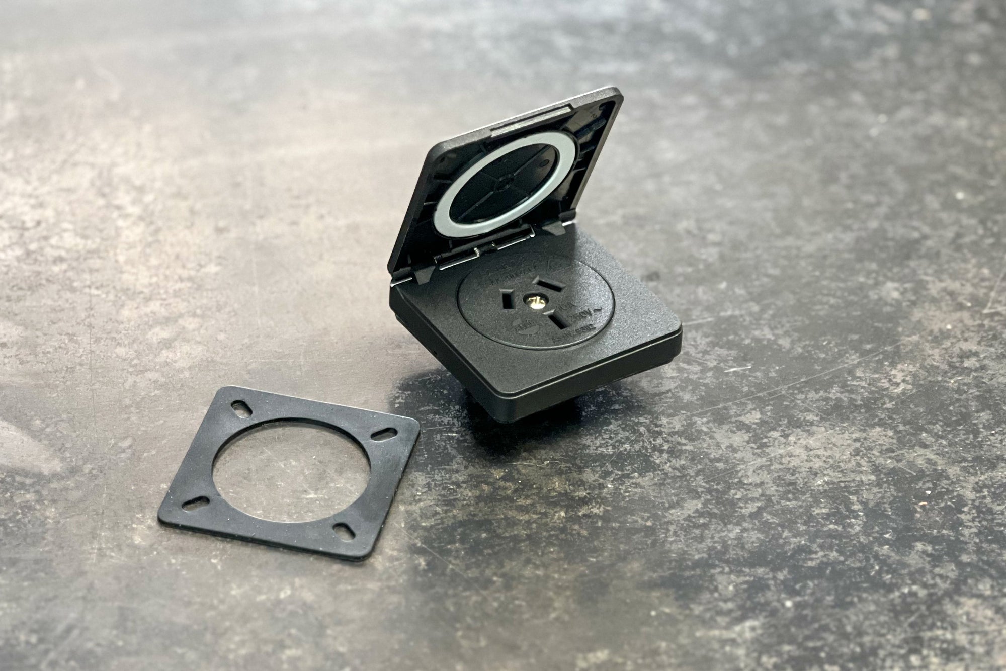240V caravan outlets, black flip cover and mounting plate on a textured surface.
