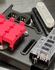 Close-up of a black metal mounting bracket with bright pink connector blocks, a translucent white cylindrical component, and a clear plastic multi-pin socket on a metallic gray surface.