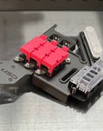 A close-up of a mechanical component or hardware part with a bright pink plastic section, black metal base, silver screws, and a clear plastic cover, photographed on a brushed metal surface.