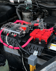 A car battery jump starter or auxiliary starter kit with bright pink and red cables, mounted on a vehicle engine bay.